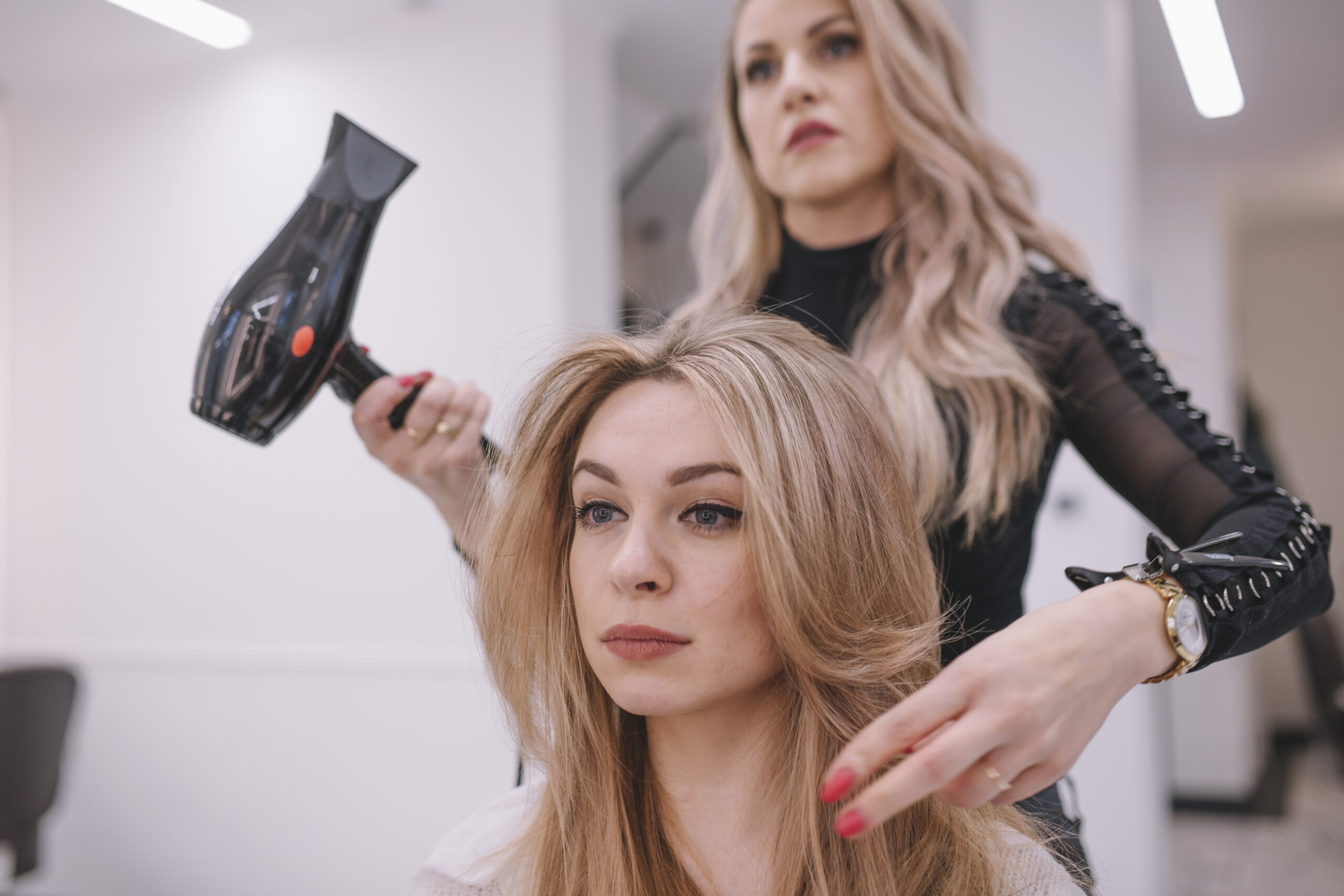 fryzjerka z suszarką w dłoni modeluje włosy młodej kobiecie