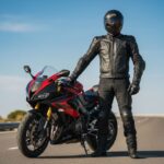 Mężczyzna w pełnym ubraniu motocyklowym stoi przy sportowym motocyklu na tle nieba i drogi.
